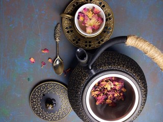 A cup of Rose tea with a metal tea pot.