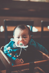 Little baby boy with pacifier sitting in high chair in restaurant