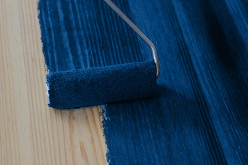 Painting wood board with roller brush with classic blue color - color of the year 2020