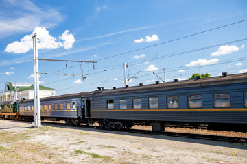 Train on railroad passing station with yellow building and blue sky with clouds.