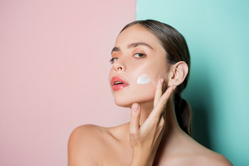 Portrait of beautiful young lady touching cheek with hand applying face cream. Selfcare routine and healthy mood. Pure smoothed skin and natural beauty concept.