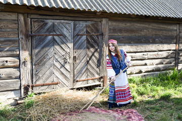 Girl works in the village. National Belarusian dress with embroidery and national pattern. Ancient wooden shed and old a equipment for labor. Belarusian girl. History and traditions of Belarus.