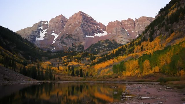 Maroon Bells morning sunrise time lapse with trees water reflection in Aspen, Colorado with rocky mountain and autumn yellow foliage panoramic view