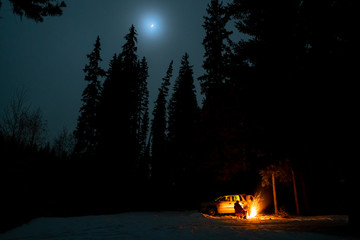 People camping under starry sky near campfire in winter in remote landscape in  Canada