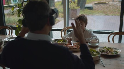 Man in virtual reality glasses in cafe with son - Powered by Adobe