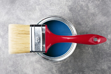 Can of classic blue paint with red brush on gray background. Top view.