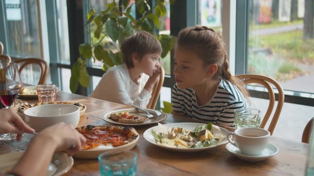 Girl talk to mother, who cuts the pizza and puts a piece of it in plate