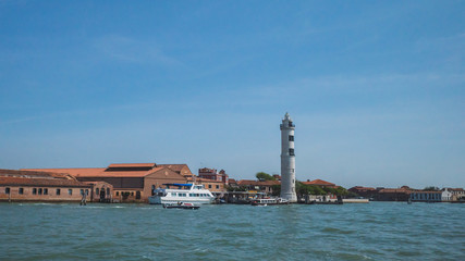 Fototapeta na wymiar Lighthouse and buildings by water, in Murano, Venice, Italy
