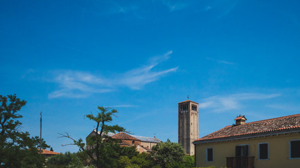 Bell tower of Cathedral of Santa Maria Assunta over buildings and trees in Torcello, Venice, Italy
