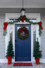 Navy blue front door of contemporary new construction siding gray home decorated for Christmas holidays with wreath trees and garland © Ursula Page