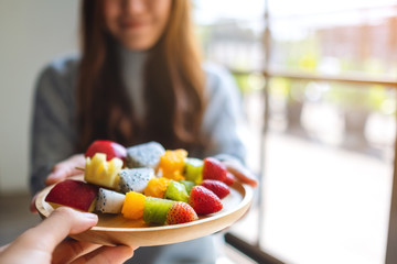 Closeup image of people giving a wooden plate of fresh mixed fruits on skewers to a woman