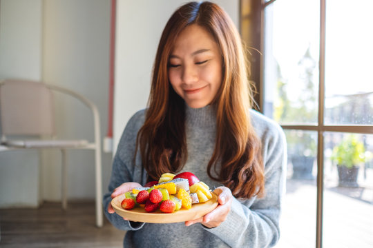 Closeup image of an asian woman holding a wooden plate of fresh mixed fruits on skewers