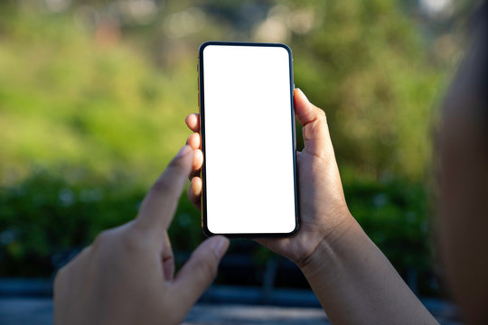 Mockup image of a hand holding and showing smartphone with blank white screen in front of the garden with bokeh light background.