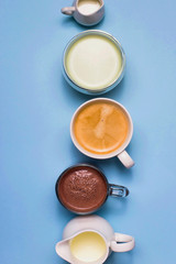 Classic blue background with different types of hot drinks - coffee, matcha, cocoa and white creamers with milk and cream.