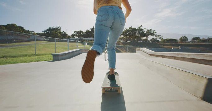 Stylish girl skateboarding in a skatepark at sunrise backlit, tracking shot of a girls legs riding a skateboard