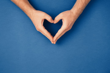 Male hands in shape of heart on classic blue background. Healthcare, chirty and Valentine's Day,...