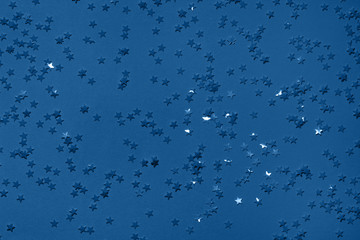 Photography on the theme of the trend color 2020. Sequins on a dark blue background with confetti as asterisks.