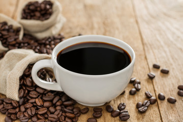 Black coffee in a white coffee cup and roasted coffee beans placed on a wooden table top view