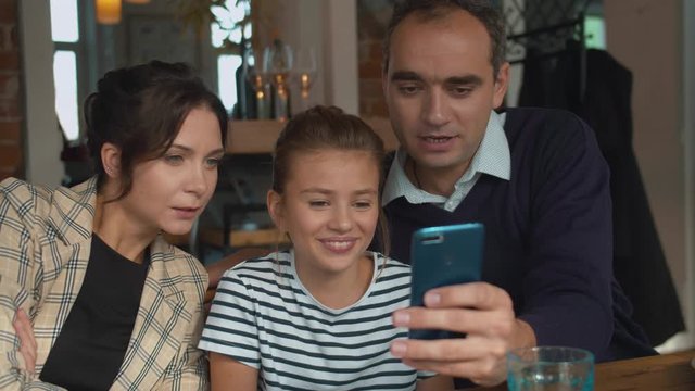 Parents and daughter look at photo on phone in a cafe