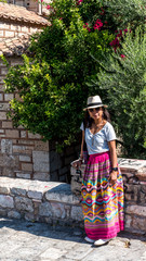 Asian woman in white t-shirt  in Athens in white hat and sarong leaning on stone wall in front of church