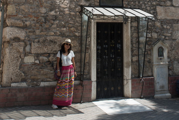 Asian woman in white t-shirt  in Athens in white hat and sarong standing in front of small Greek Orthodox church