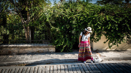 Asian woman in white t-shirt in Athens in white hat and sarong looking down at cat