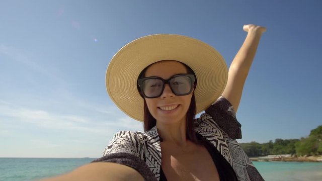 smiling girl in sunglasses and straw hat shooting selfie video on ocean beach,