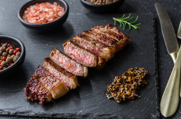 New york strip loin beef steak meat with chimichurri sauce against black stone background