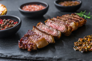 New york strip loin beef steak meat with chimichurri sauce against black stone background - obrazy, fototapety, plakaty