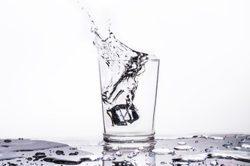 Water splashes out of the glass on a white background