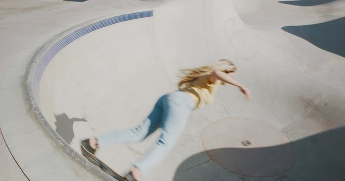 Stylish skater girl skateboarding doing a big carve around the top of a concrete bowl in slow motion, old vintage filmy look skateboarding girl