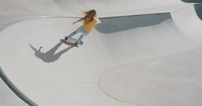Stylish retro girl skateboarding doing a surf style turn around a concrete bowl feature in a skatepark at sunrise in slow motion, skateboarder girl ripping