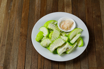 Sliced Pickled guava on white plate with salt and ground red or green peppers, eaten as a condiment