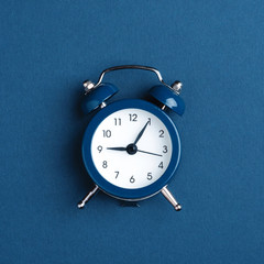 Classic alarm clock on blue background. Minimal styled photo.