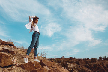 Beautiful girl in a white shirt and blue jeans posing on the rock. Outdoor shot. Summer vacation concept.