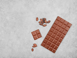 Bar of milk chocolate and cocoa beans on gray stone background