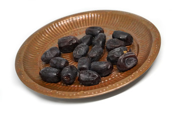 Dry dates fruit in a copper dish closeup on white background, Dried date palm fruits or kurma, ramadan food.