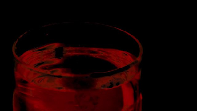 Red drops in water glass in slow motion with black background.
