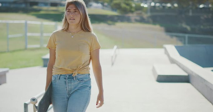 Medium portrait of a blonde skater girl walking holding her skateboard, urban skate surf lifestyle moments
