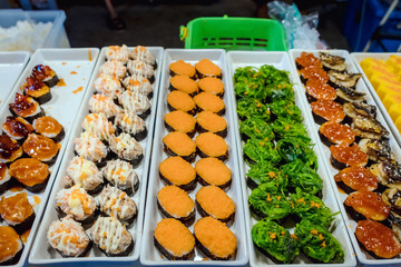 Rows of japanese sushi food. Maki ands rolls with tuna, salmon, shrimp, crab and avocado. Top view of assorted sushi in black plastic container being sale at market. Selective focus.