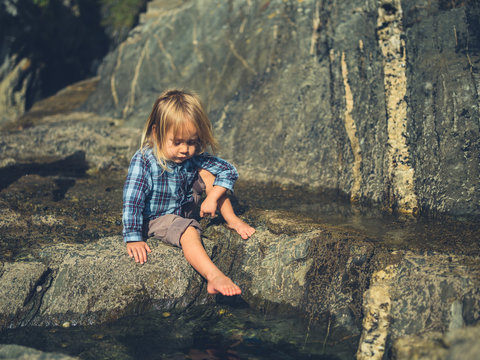Little toddler dipping his feet in rock pool