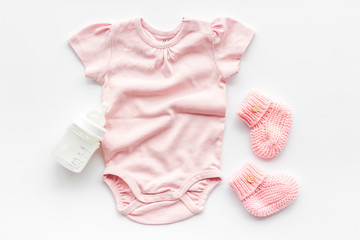 Pink bodysuit for baby girl near children's things on white background top-down