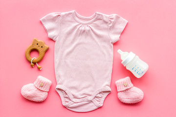 Pink bodysuit for baby girl near children's things on pink background top-down