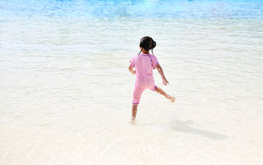 Fototapeta premium Little Asian child girl having fun and running into aqua park on holidays. Back view kid enjoys in big swimming pool outdoor.