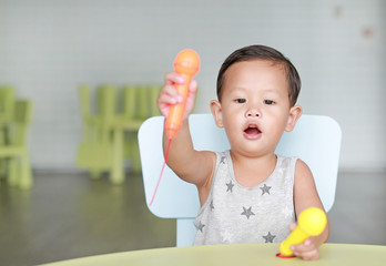 Portrait of little Asian baby boy sing a song by plastic microphone at children room.