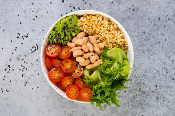 Fototapeta na wymiar A plate of fresh salad with white beans, bulgur, cherry tomatoes and avocado, decorated with black sesame seeds. Horizontal photo with copy space, top view