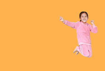 Happy and smile little Asian child girl in pink tracksuit or sport cloth jumping on air isolated on yellow background with copy space. Freedom kid movement concept.