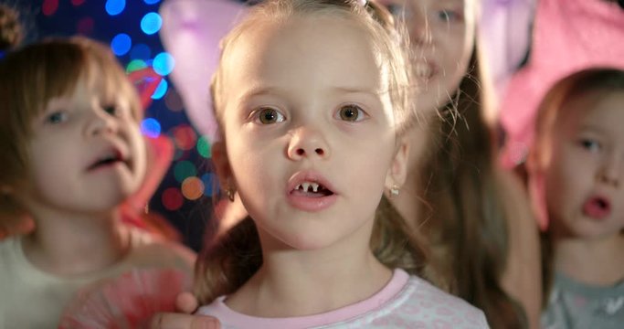 Portrait of a five year old girl in the foreground sings a song in a group of children.