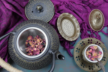 A cast iron teapot kettle with a cup of Rose tea and some rose petals