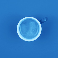 Top view of fresh brewed coffee in ceramic cup over background in blue color.